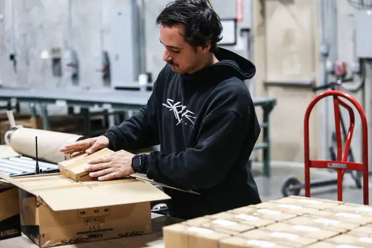 A guy wearing a Skar Audio hoodie, loading a box in a warehouse